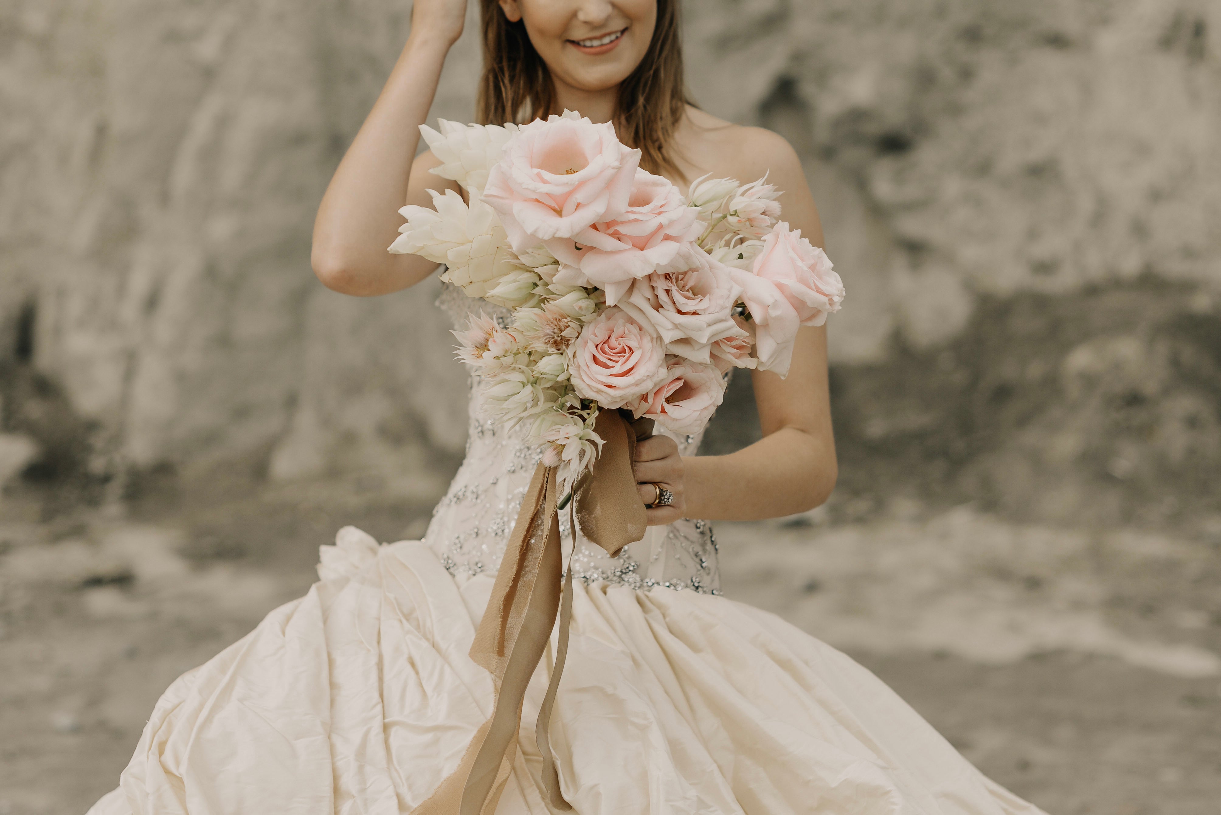 Braut im cremefarbenen Kleid hält romantischen Brautstrauß mit rosafarbenen Rosen – stilvolles Hochzeitsfoto mit floralen Details