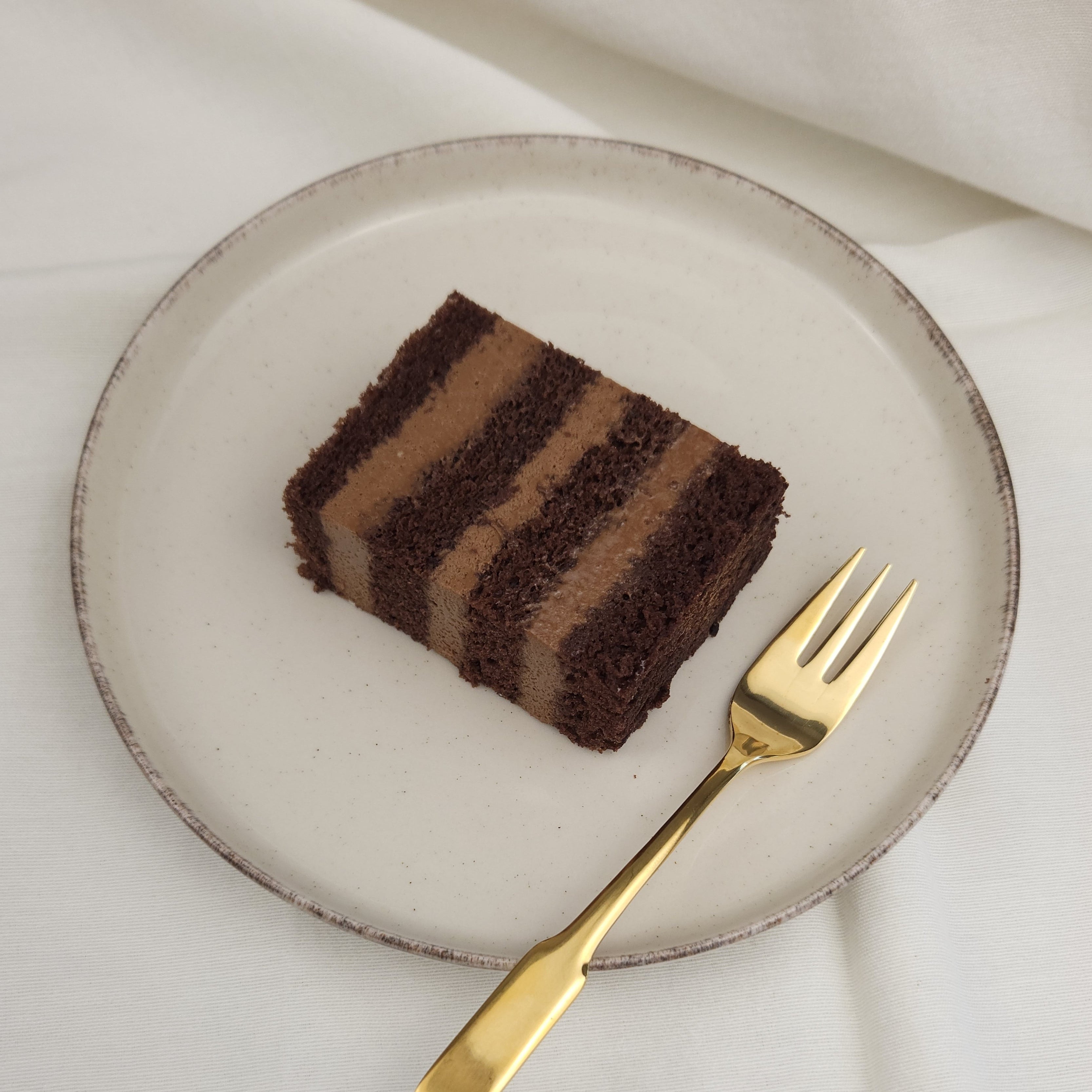 Stück intensiver Schokoladentorte mit luftiger Mousse auf Keramikteller und goldener Kuchengabel – perfekt für Schokoliebhaber