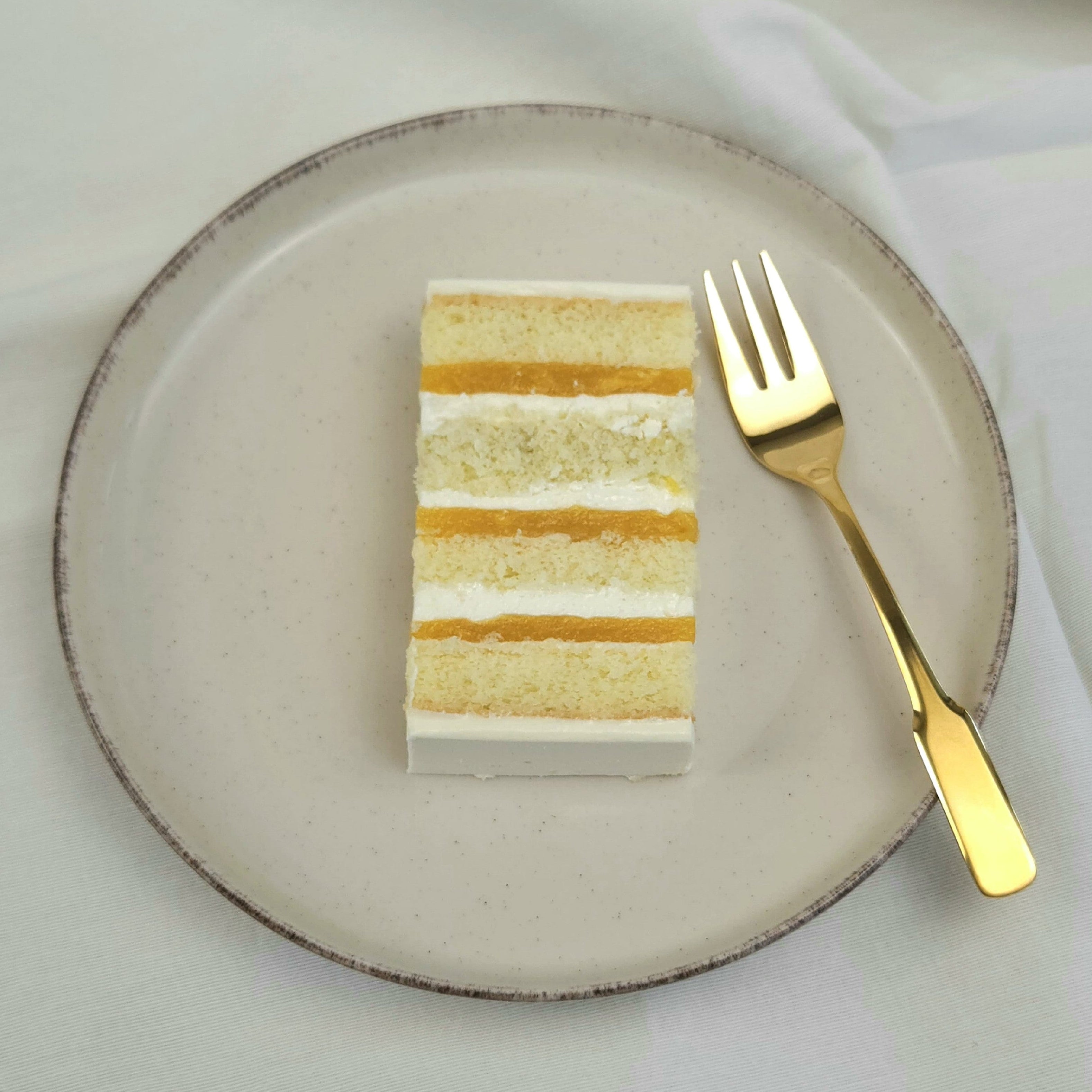 Stück Coconut-Mango-Passion Torte mit exotischer Fruchtschicht und Cremefüllung auf Keramikteller mit goldener Kuchengabel
