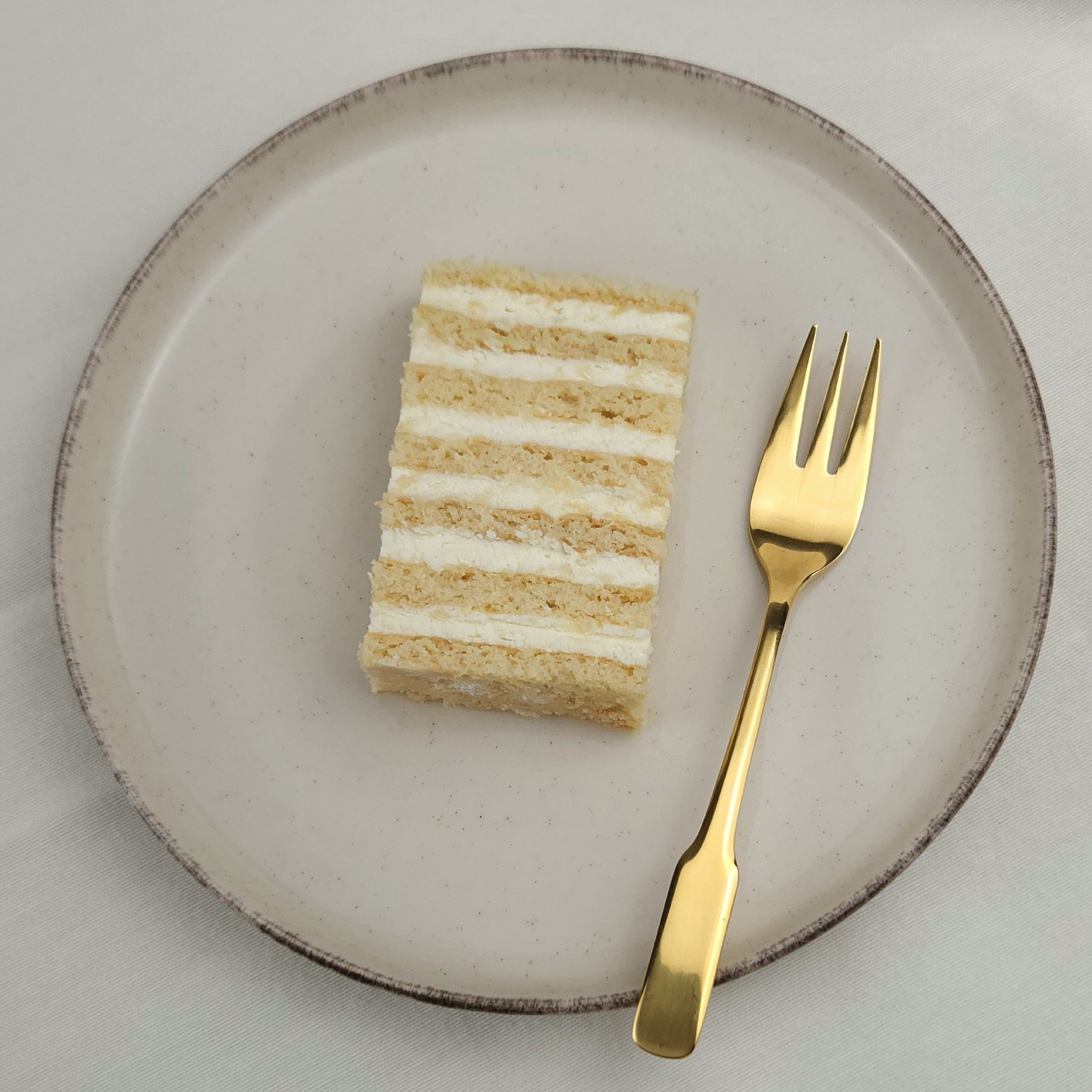 Klassischer Honigkuchen mit cremiger Schicht auf Keramikteller und goldener Kuchengabel – süß, leicht und nostalgisch