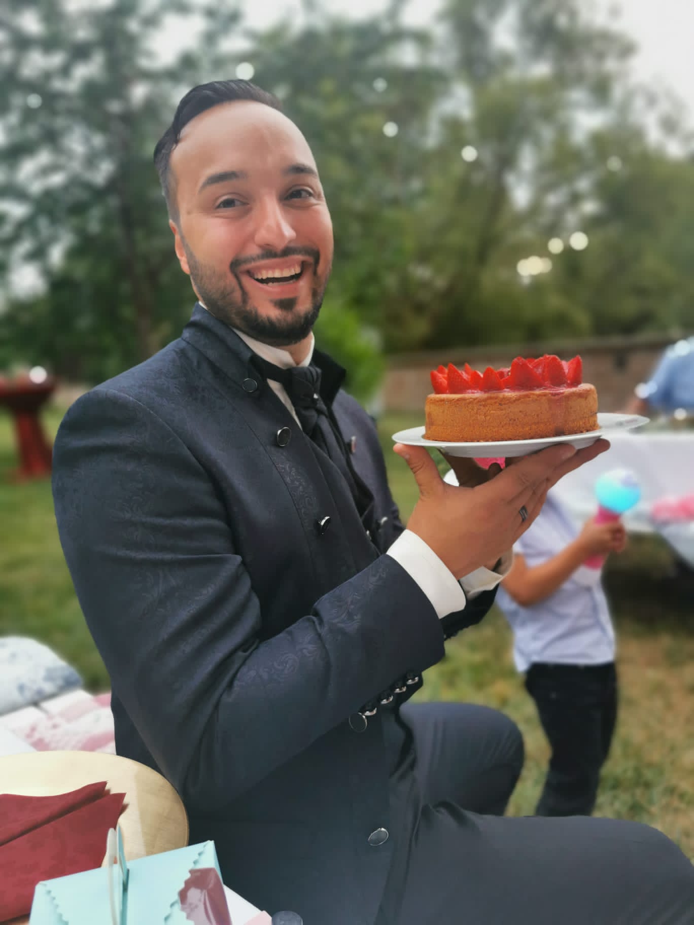 Lächelnder Mann im festlichen Anzug hält Erdbeertorte bei Outdoor-Feier – handgemachter Kuchen, ideal für Events und Hochzeiten in Berlin