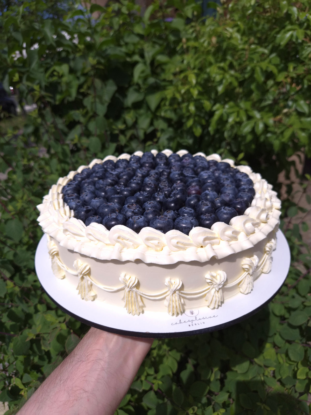 Runde Torte mit Blaubeeren, weißen Cremetupfen und seitlichen Girlanden