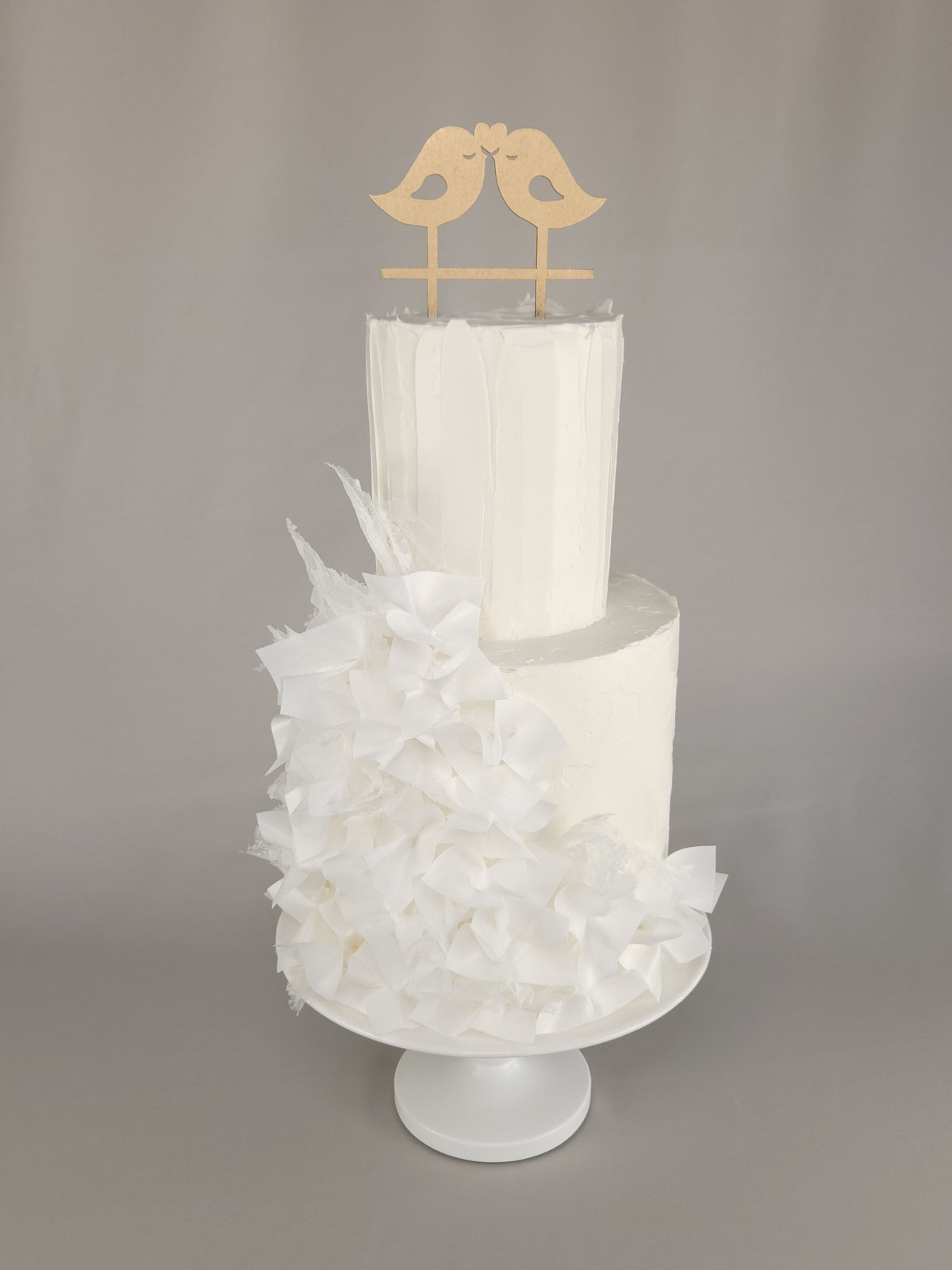 Zweistöckige weiße Hochzeitstorte mit üppiger weißer Blütendekoration und goldfarbenem Vogelpaar als Topper