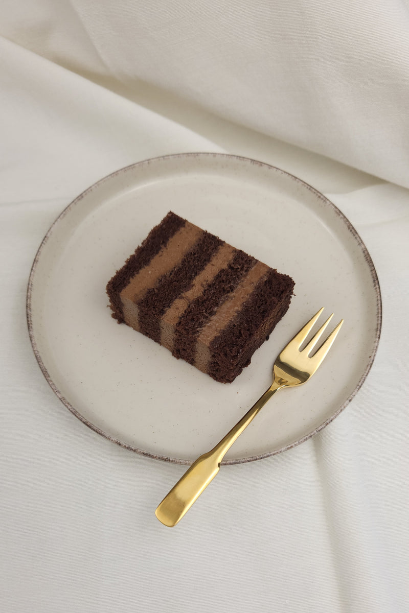 Stück intensiver Schokoladentorte mit luftiger Mousse auf Keramikteller und goldener Kuchengabel – perfekt für Schokoliebhaber