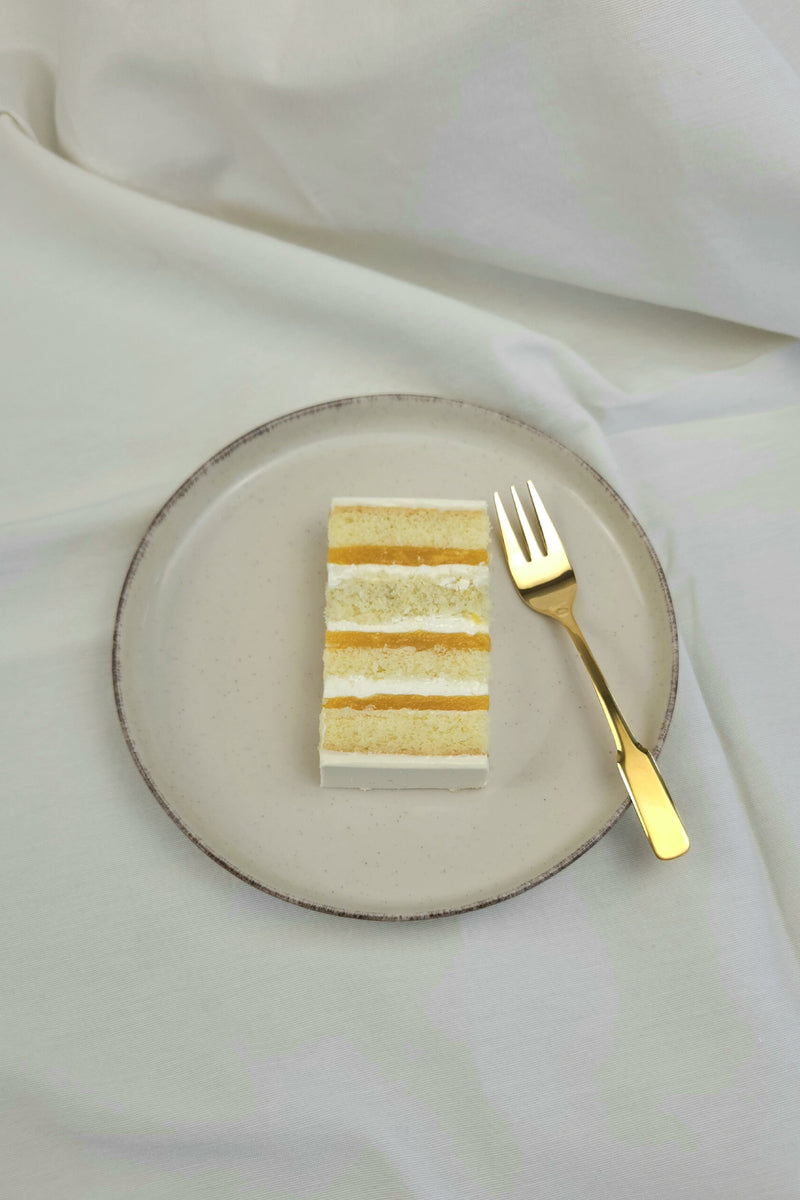 Stück Coconut-Mango-Passion Torte mit exotischer Fruchtschicht und Cremefüllung auf Keramikteller mit goldener Kuchengabel