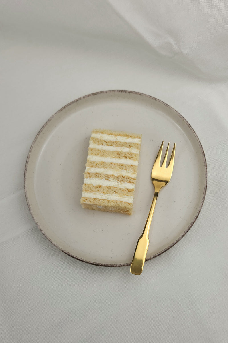Klassischer Honigkuchen mit cremiger Schicht auf Keramikteller und goldener Kuchengabel – süß, leicht und nostalgisch