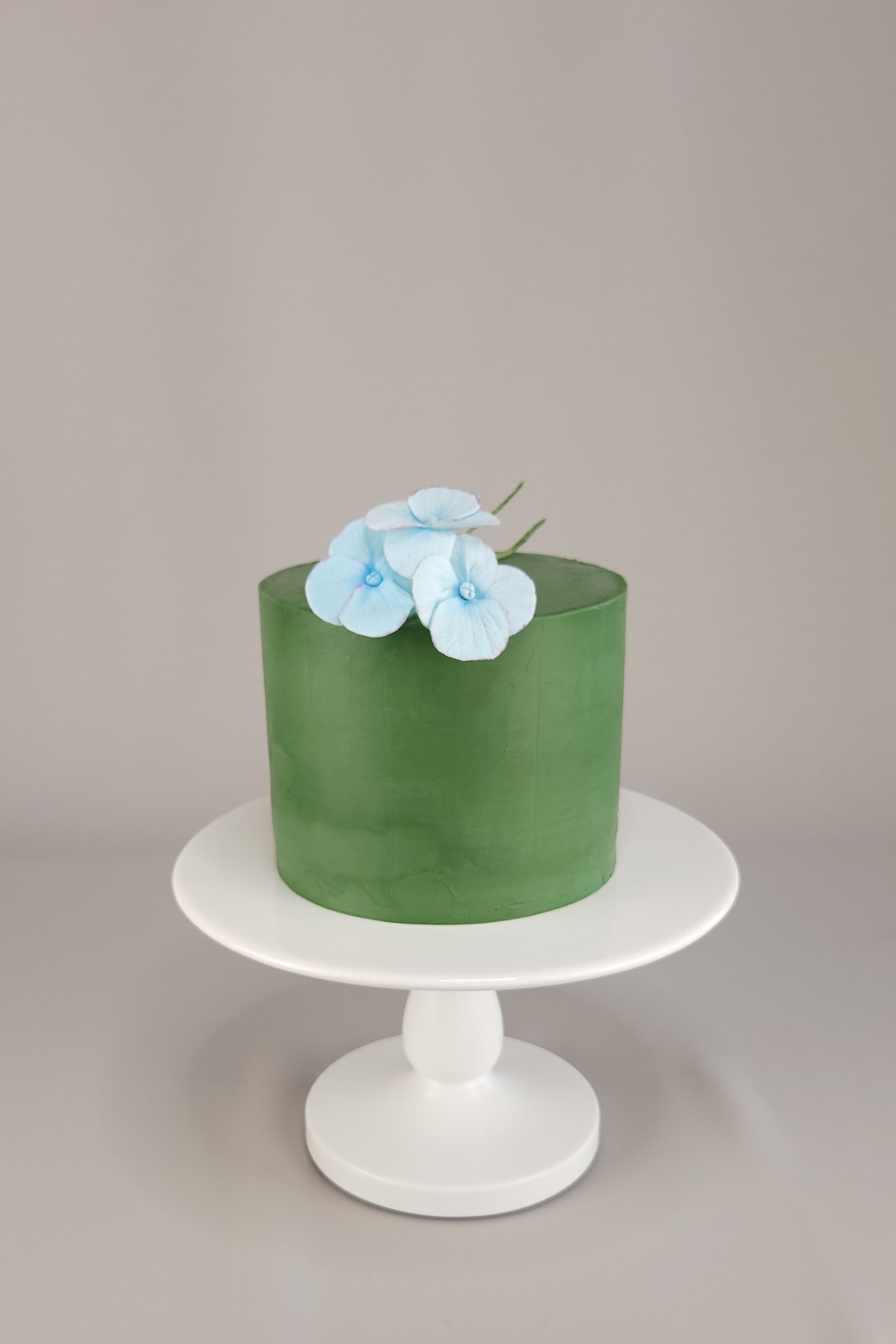 Einstöckige Torte mit grünem Ganache-Überzug und drei handgefertigten Hortensienblüten aus Zucker-Blütenpaste – elegante Torte aus Berliner Meisterkonditorei.