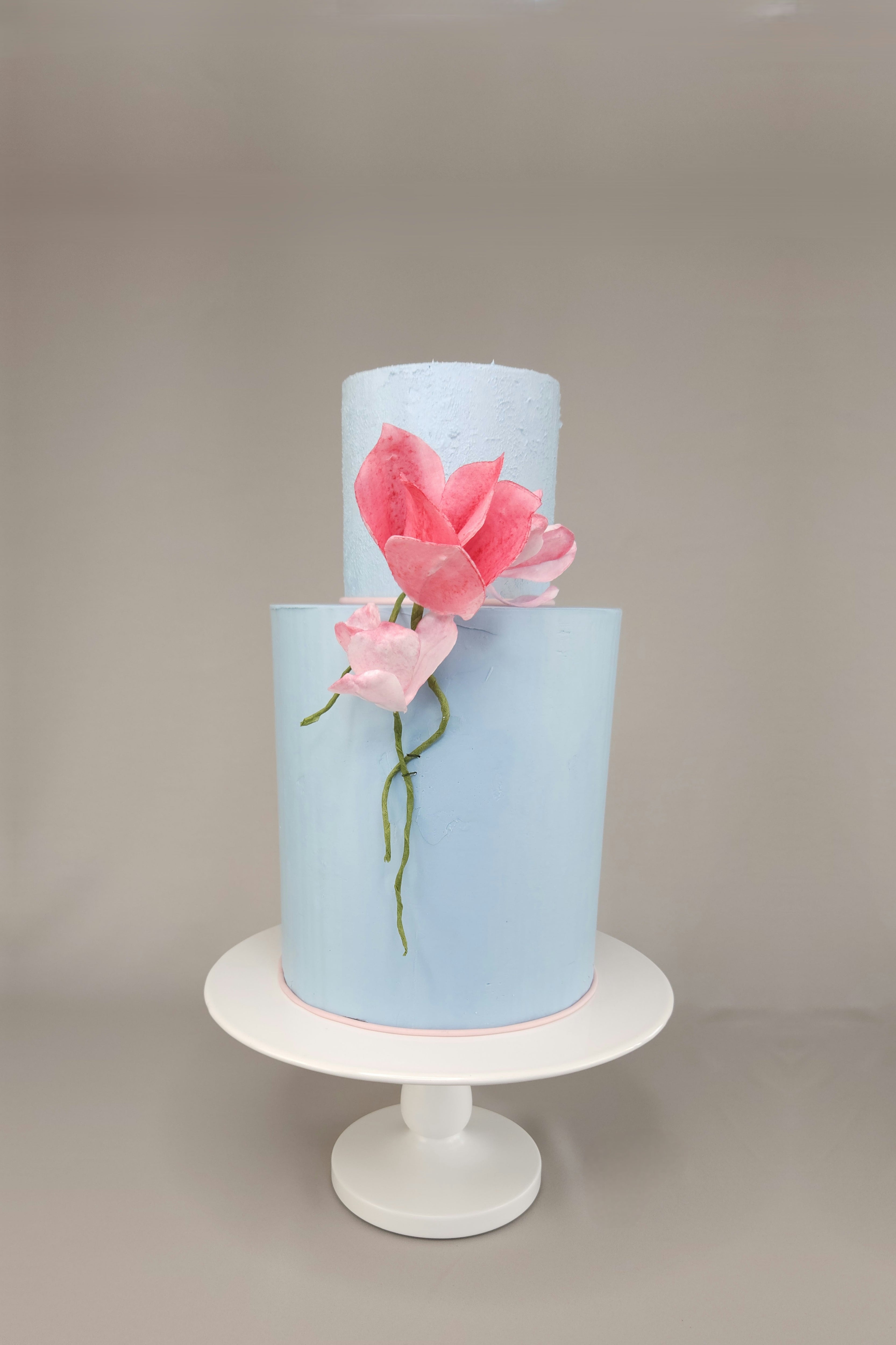 Zweistöckige Design-Torte mit hellblauer Ganache und handgefertigten rosa Magnolien aus essbarem Papier – Hochzeitstorte kaufen in Berlin.