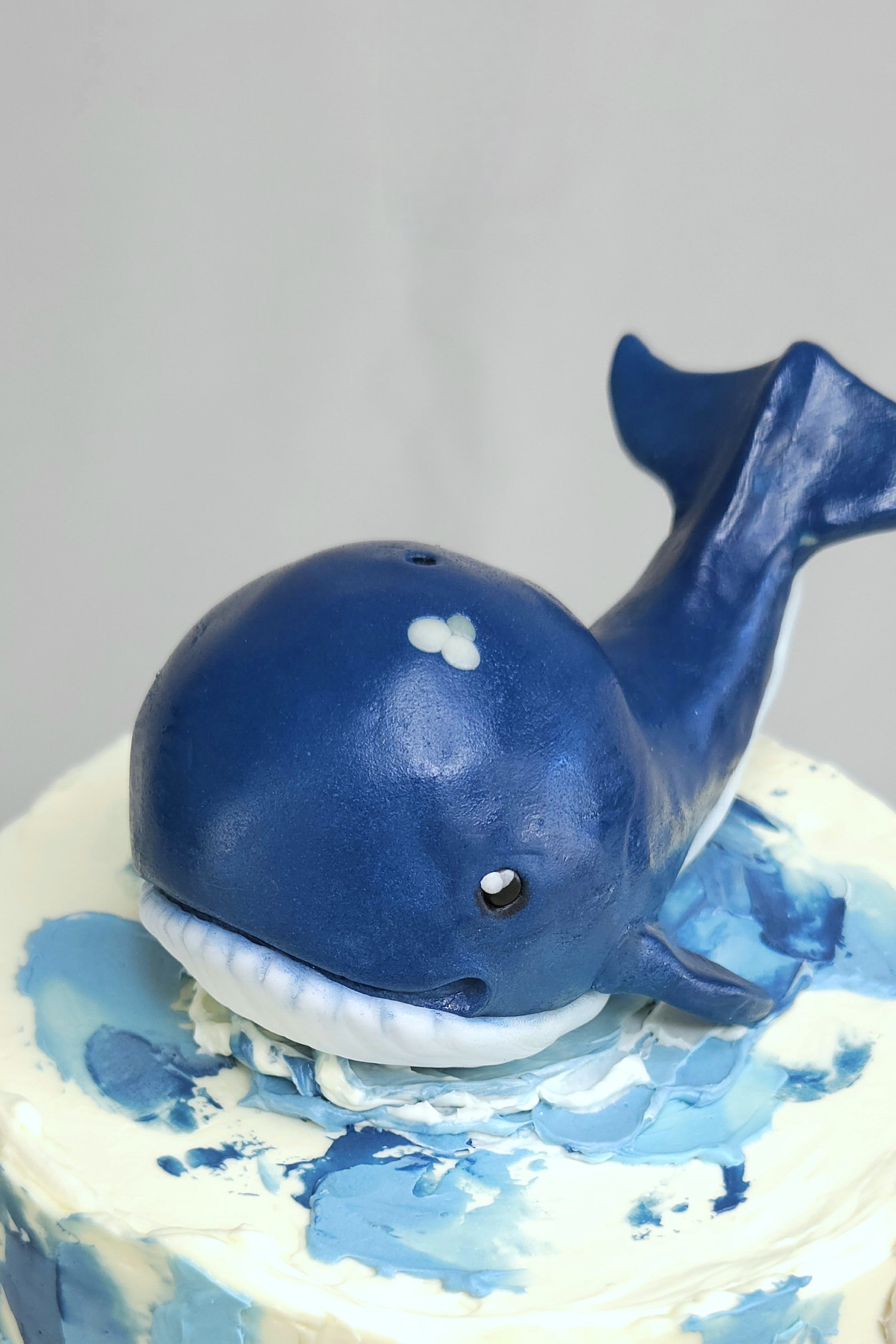 Handgeformter blauer Wal aus Puffreis, Marshmallow und Modellierschokolade auf maritimer Design-Torte mit cremeblauer Ganache – perfekt für Kinderfeste oder Taufen.