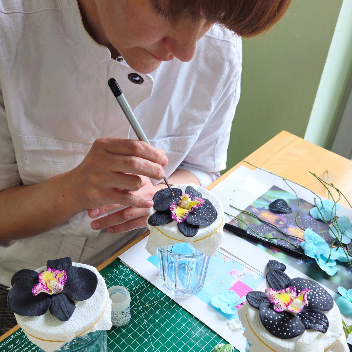 Konditorin bemalt handgefertigte schwarze Zucker-Orchideen mit feinem Pinsel – detailreiche Handarbeit für exklusive Design-Torten.